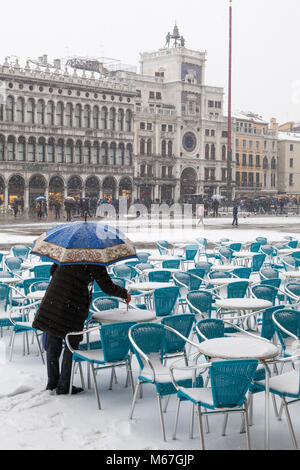 Venice, Veneto, Italy 1st March 2018. Bad weather in Venice today with sub-zero temperatures between minus 3 and minus 2 and continuous snow falling throughout the day caused by the Beast from the East, or the Siberian front from Russia sweeping across Europe.  woman under an umbrella writing i the snow on a restaurant table in Piazza San Marco. Stock Photo