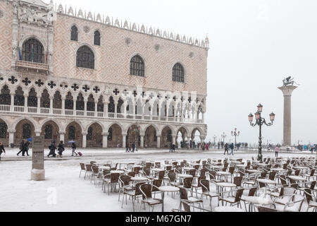 Venice, Veneto, Italy 1st March 2018. Bad weather in Venice today with sub-zero temperatures between minus 3 and minus 2 and continuous snow falling throughout the day caused by the Beast from the East, or the Siberian front from Russia sweeping across Europe.  Tourists with suitcases hurrying through Piazza San Marco in front of the Doges Palace and restaurant tables and chairs.