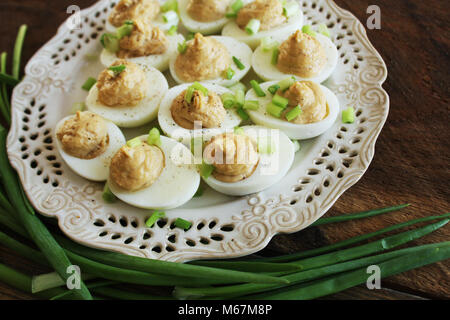 Deviled eggs with cod livers with leek on white plate. Rustic wooden table Stock Photo