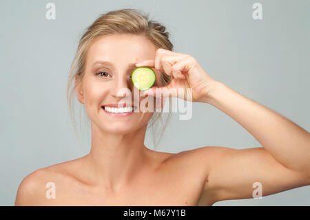 Beauty - the natural way. Facial mask with cucumber. Beautiful woman is holding cucumber slices while Stock Photo