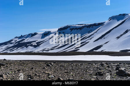 Dramatic Snow Covered Volcanic Ridge against a Blue Sky, Western Highlands, Iceland with sparse vegetation Stock Photo