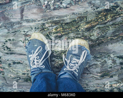 The feet of a young man wearing trainers standing on the rocks Stock Photo