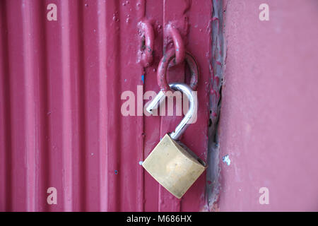 Unlocked brass padlock on a red metal door Stock Photo