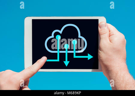 Man holding a tablet device and cloud computing communication icon to download stored data, touching the screen with a finger with blue sky in backgro Stock Photo