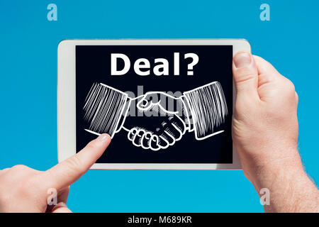 Man holding a tablet device showing illustration of deal teamwork handshake hands as agreement concept with blue sky in background. Stock Photo
