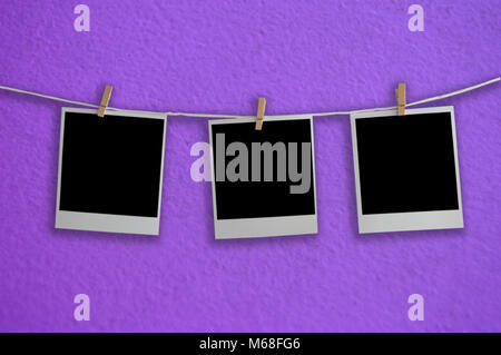 Three frames polaroid hanging on a rope behind the lilac background Stock Photo