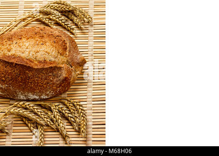 Toasty Organic Loaf of Bread with wheat on wooden plank isolated on white. Stock Photo