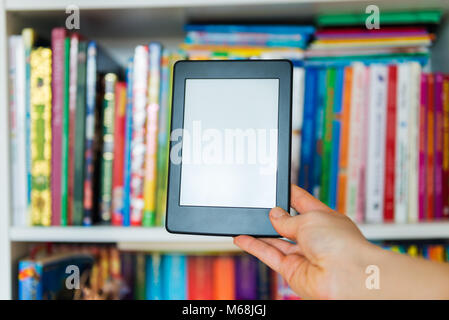 Ebook or digital reading tablet device, on the background is the shelf with bright real books Stock Photo