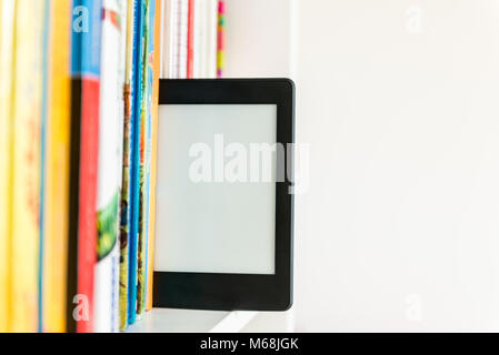 Ebook or digital reading tablet device standing on the shelf with bright real books Stock Photo