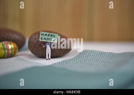 happy Easter words with chocolate Easter eggs and cute miniature person figurine Stock Photo