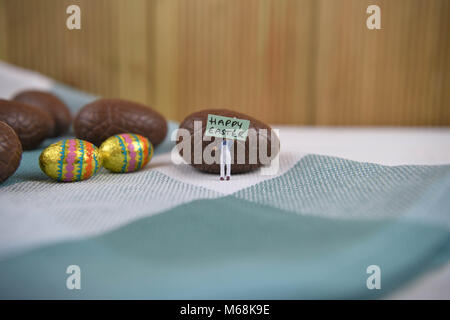 happy Easter words with chocolate Easter eggs and cute miniature person figurine Stock Photo
