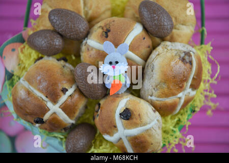 Easter food in a basket with hot cross buns and chocolate Easter eggs with Easter bunny decorations Stock Photo