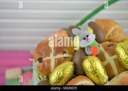 Easter food in a basket with hot cross buns and golden chocolate Easter eggs with Easter bunny decoration Stock Photo