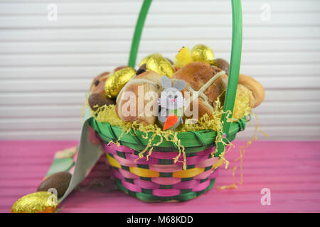 Easter food in a basket with hot cross buns and golden chocolate Easter eggs with Easter bunny decoration Stock Photo