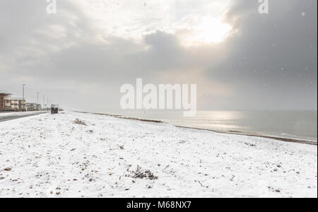 Snow covered deserted beach with the sun rising though clouds in Winter in Littlehampton, West Sussex, England, UK. Stock Photo