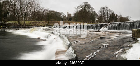 Wier on the River Wenning with Hornby Castle beyond on a cold, icy day. Stock Photo