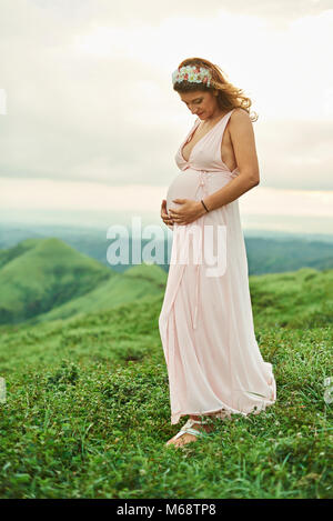 Pregnant woman stand on grass looking and hold hands on belly Stock Photo