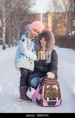 a young mother leads her daughter from school, the family smiles, children have fun, the family walks in the winter, go on the road. Stock Photo