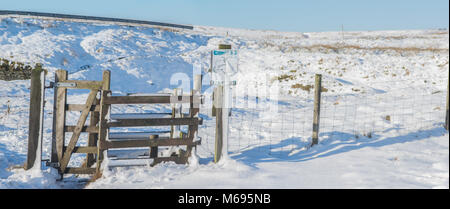 Moorside footpath gate and stile on the West Pennine Moors under the bright winter sun after a heavy fall of snow Stock Photo
