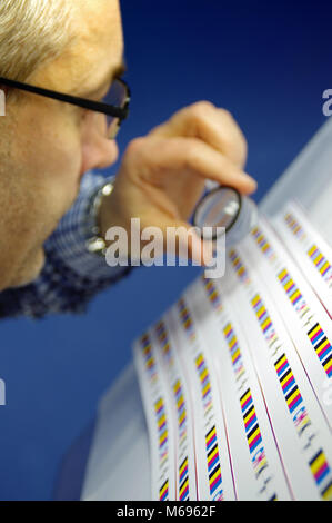 Man using magnifier lens for checking quality. Print test controlling cmyk and registration mark on printout. Stock Photo