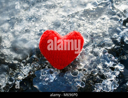 warm red knitted heart lying on the cold glittering ice Stock Photo