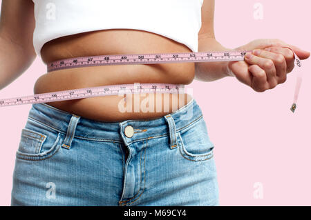 Overweight woman with tape measure around waist on pastel pink background Stock Photo