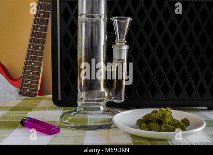 A transparent crystal bong weed, a plate full of marihuana and a purple lighter with a red electric guitar and amplifier in the background. Inspiring  Stock Photo