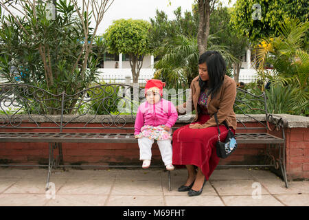 A young ethnic indigenous Ixil Maya woman sitting on a bench with her baby daughter in a park. San Juan Cotzal, Ixil Triangle, Guatemala. Stock Photo