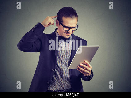 Young formal man in glasses using tablet and scratching head in misunderstanding. Stock Photo