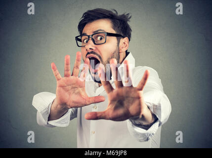 Young scared man in shirt holding hands in front of face and screaming in panic. Stock Photo