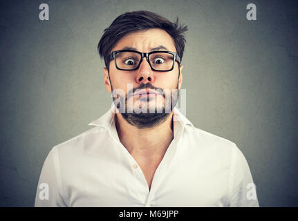 Young bearded man in glasses looking at camera with expression of panic on gray background. Stock Photo