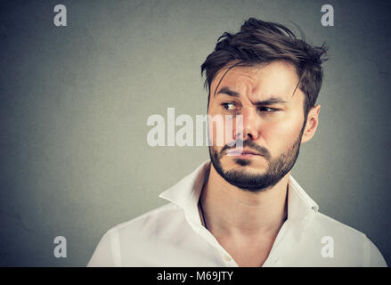 Handsome bearded man in white shirt looking away with suspicion on gray background. Stock Photo