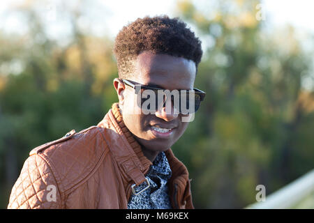 A handsome young black man in sunglasses and a leather jacket on a fall day Stock Photo