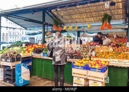 Woman buying vegetables and fresh produce  at the Rialto Market, Rialto Mercato, San Polo, Venice, Italy overlooking the Grand Canal on a misty cold w Stock Photo