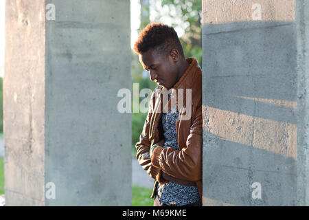 Handsome thoughtful young black man leaning on a wall looking down Stock Photo
