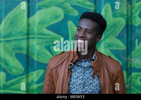 Handsome young black man smiles in front of wall painted with leaves Stock Photo