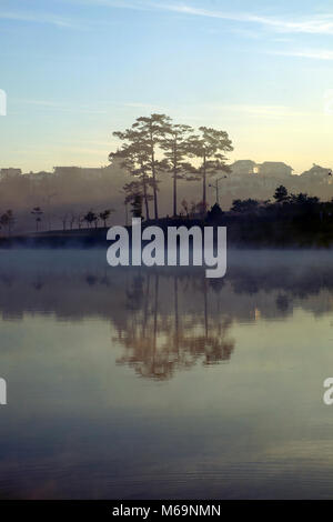 Beautiful landscapes of Da Lat city at morning with lake in fog, pine tree reflect on water, scenery in purple, this place is romantic destination for Stock Photo