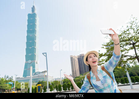 Young modern fashion Asian woman lady having a selfie in front of the brilliant sight of Taipei tallest building. She raises up her hands like to intr Stock Photo