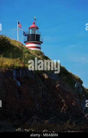 West Quoddy Head Lighthouse, painted in red and white stripes like a candy cane, overlooks a rocky cliff. The beacon resides in Lubec, Maine. Stock Photo