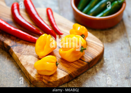 Red and yellow hot peppers on cutting board with green peppers in a bowl Stock Photo