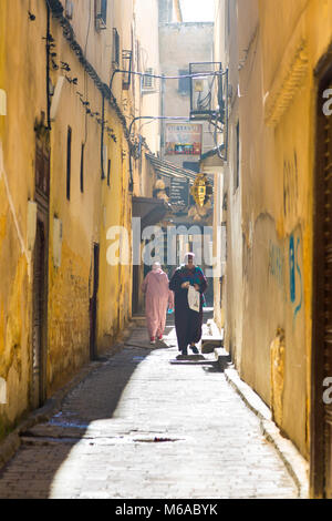 Moroccan women in traditional muslim clothing walking down a narrow street in the medina in Fes, Morocco Stock Photo