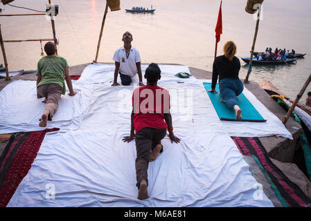 A group of people practicing yoga by the Ganges River in the early morning in Varanasi, India. Stock Photo