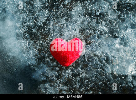 warm red knitted heart lying on the cold glittering ice Stock Photo