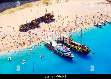 Boats anchored at Navagio beach, Zakynthos. Famous shipwreck on the beach and tourist bathing in the sun. Stock Photo