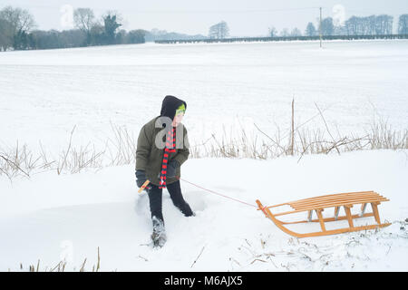 Eight year old boy in the snow using a traditional wooden toboggan or sledge, Medstead, Alton, Hampshire, England, United Kingdom. Stock Photo