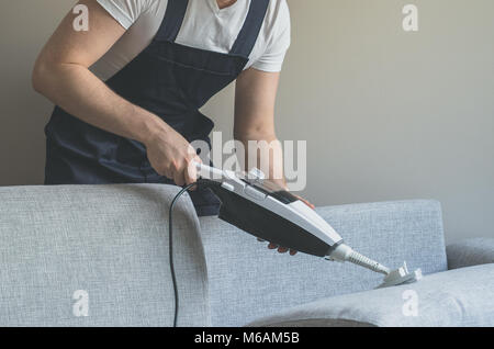 Man in uniform cleaning fabric of the sofa with dry steam cleaner. Stock Photo