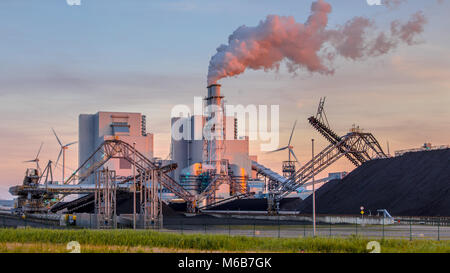 Heavy industrial coal powered electricity plant with pipes and smoke in orange light of setting sun Stock Photo