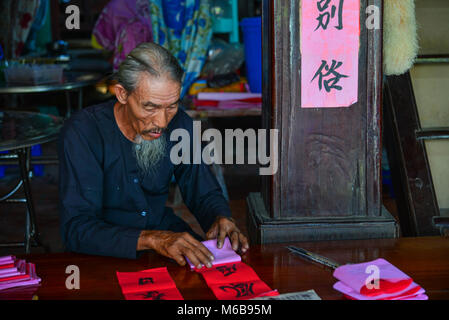 Vung Tau, Vietnam - Feb 6, 2018. An old man writing Chinese calligraphy on red paper at an old village in Vung Tau, Vietnam. Stock Photo