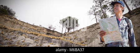 Composite image of low angle view of smiling hiker holding map Stock Photo