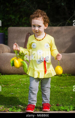 Cute toddler girl in yellow dress with lemons in both hands Stock Photo